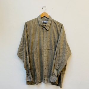 May include: A long-sleeved, striped button-down shirt in a light brown color. The shirt is hanging on a wooden hanger against a white wall.