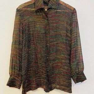 May include: A sheer button-down shirt with horizontal stripes in various colors, including red, yellow, green, and black. The shirt has long sleeves with buttoned cuffs and a classic collar. The garment is hanging on a wooden hanger.