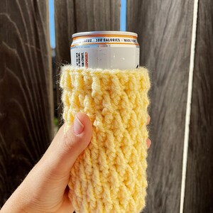 May include: A yellow crocheted can cosy, ideal for keeping your drink cold. The cosy is made with a simple stitch pattern and is easy to make.
