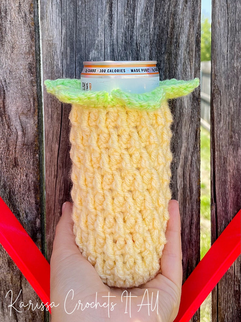 May include: A yellow crocheted can cooler with a green crocheted top. The cooler is holding a silver can with the text "2g CARBS - 100 CALORIES - MADE PURE" on it.