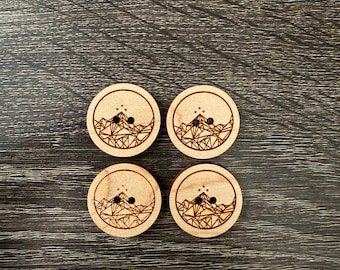 May include: Four wooden buttons with a geometric mountain design and a star pattern. The buttons are light brown and have two holes each.