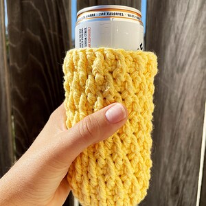 May include: A yellow crocheted can cosy, ideal for keeping your beverage cold. The cosy is made with a simple stitch pattern and is a great way to add a touch of personality to your drink.