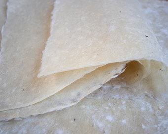 May include: A stack of handmade paper sheets with a natural, off-white color and a slightly textured surface.