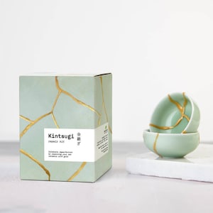 May include: A Kintsugi repair kit with a box and two small bowls. The box is light green with gold-colored lines, and the text "Kintsugi repair kit" is on the front. The bowls are light green with gold-colored repair lines.