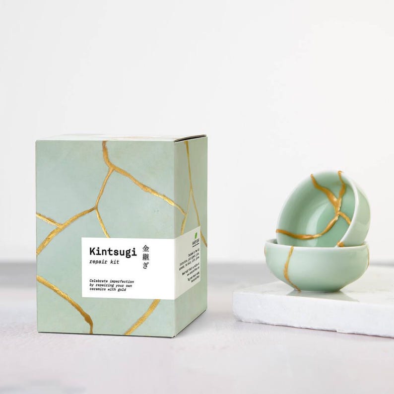 May include: A Kintsugi repair kit with a box and two small bowls. The box is light green with gold-colored lines, and the text "Kintsugi repair kit" is on the front. The bowls are light green with gold-colored repair lines.