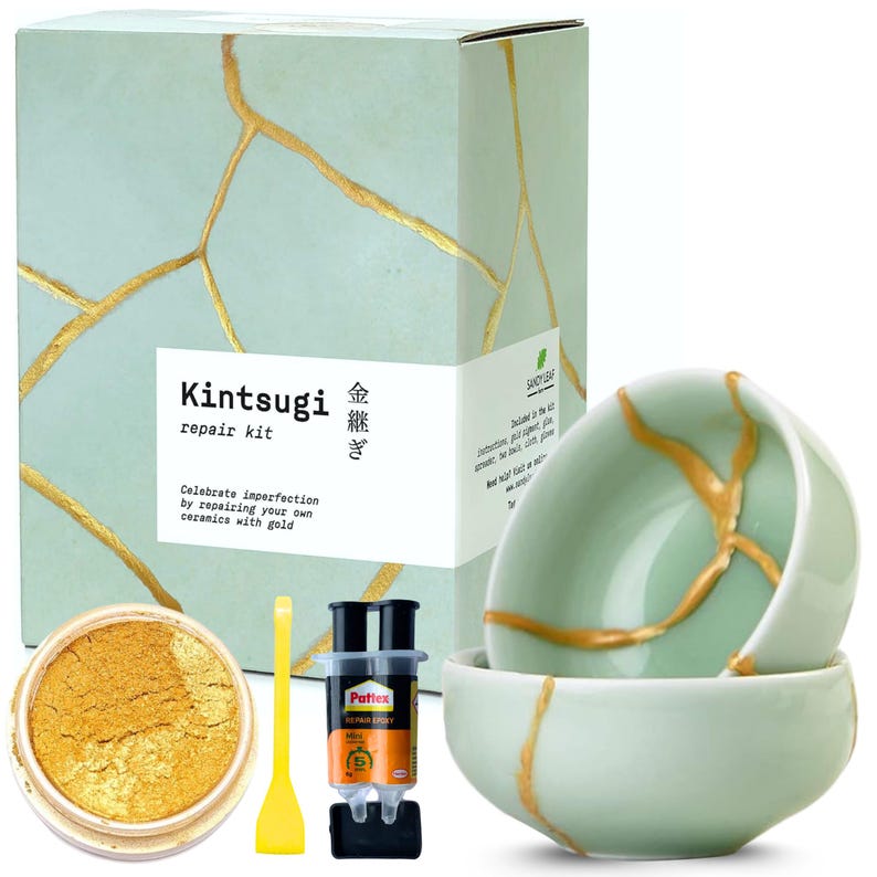 May include: Kintsugi repair kit with gold powder, epoxy, and a yellow spatula. The kit includes two light green ceramic bowls with gold-colored repair lines. The box reads "Kintsugi repair kit" and "Celebrate imperfection by repairing your own ceramics with gold."