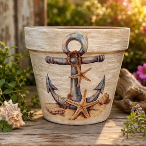 May include: A tapered terracotta plant pot with a distressed off-white finish. The exterior features a painted illustration of a blue anchor resting on sand, adorned with two tan starfish and a small seashell at the base of the anchor.