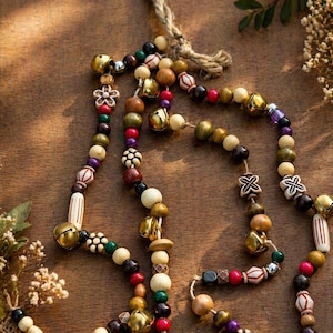 May include: A collection of beaded garlands with a rustic aesthetic. The garlands feature a variety of wooden beads in natural tones, accented with colorful beads, small bells, and decorative elements. Strung on twine, they offer a bohemian or farmhouse style.