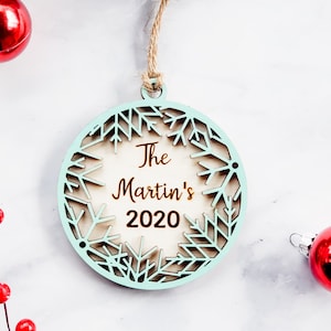 May include: A light blue wooden Christmas ornament with a snowflake design. The ornament has the text "The Martin's 2020" inscribed on it.