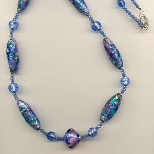 May include: A blue and pink glass bead necklace with a floral pattern. The necklace is made of small blue glass beads and larger, oval-shaped beads with a floral design.