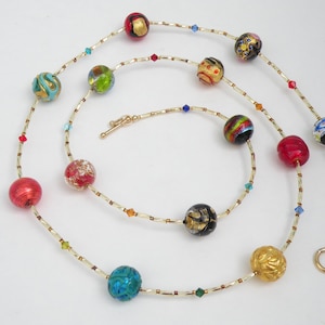May include: A long gold chain necklace with colorful glass beads. The beads are round and have different patterns and colors, including red, blue, green, and gold. The necklace has a clasp closure.