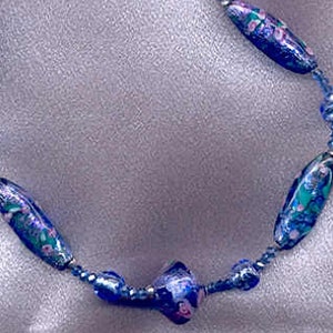 May include: A blue and white glass bead necklace with floral patterns. The necklace is made of small, round beads and larger, oval beads.