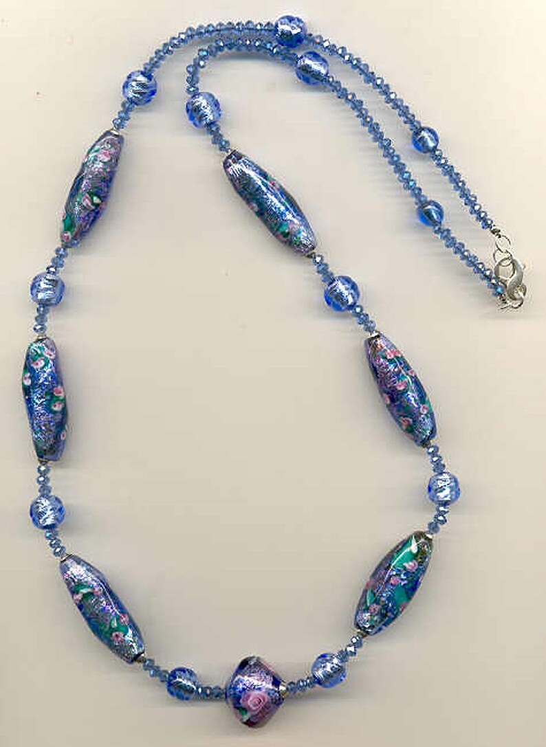 May include: A blue and pink glass bead necklace with a floral pattern. The necklace is made of small blue glass beads and larger, oval-shaped beads with a floral design.