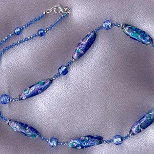 May include: A blue and purple glass bead necklace with a silver clasp. The beads are oval shaped and have a floral pattern.