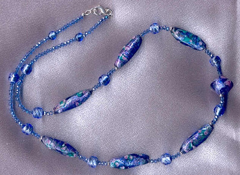 May include: A blue and purple glass bead necklace with a silver clasp. The beads are oval shaped and have a floral pattern.