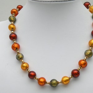 May include: A necklace made of round, multi-colored glass beads. The beads are shades of green, orange, and red. The beads are strung on a gold chain.