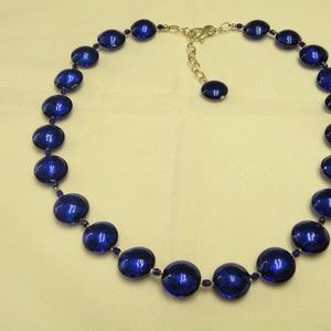 Peut inclure: Un collier compos&eacute; de grandes perles ovales bleu fonc&eacute;. Les perles sont enfil&eacute;es avec de petites perles bleues rondes et des accents m&eacute;talliques dor&eacute;s. Il poss&egrave;de un fermoir r&eacute;glable argent&eacute;.