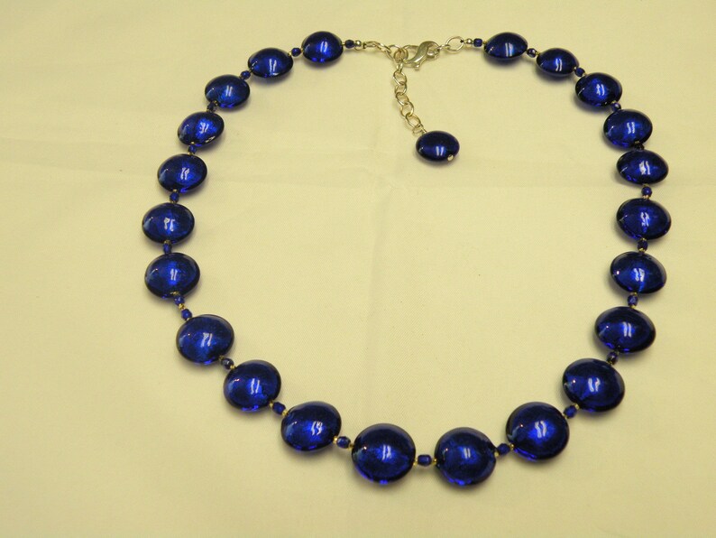 Peut inclure: Un collier compos&eacute; de grandes perles ovales bleu fonc&eacute;. Les perles sont enfil&eacute;es avec de petites perles bleues rondes et des accents m&eacute;talliques dor&eacute;s. Il poss&egrave;de un fermoir r&eacute;glable argent&eacute;.
