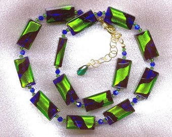 May include: A necklace featuring rectangular green and blue dichroic glass beads. The beads are connected by small blue beads and gold-colored chain. The necklace has a gold-colored clasp and a green teardrop pendant.