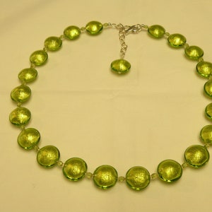 May include: A green glass necklace with round beads. The beads have a metallic sheen and are strung on a silver chain.