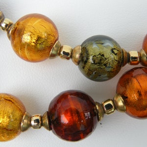 May include: A necklace made of large, round glass beads in shades of gold, brown, and green. The beads have a metallic sheen and are separated by gold-toned spacers.