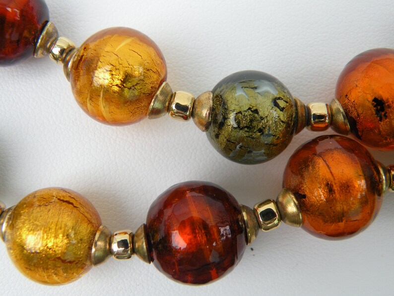 May include: A necklace made of large, round glass beads in shades of gold, brown, and green. The beads have a metallic sheen and are separated by gold-toned spacers.