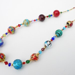 May include: A vibrant necklace with a gold chain, showcasing a series of glass beads in shades of red, blue, green, and gold. The necklace is embellished with small crystals. The beads display detailed patterns and designs.