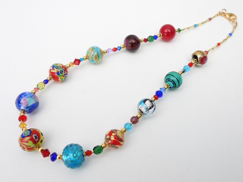 May include: A vibrant necklace with a gold chain, showcasing a series of glass beads in shades of red, blue, green, and gold. The necklace is embellished with small crystals. The beads display detailed patterns and designs.