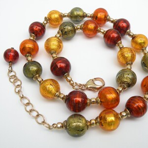 May include: A gold chain necklace with large, round, multi-colored glass beads. The beads are in shades of orange, red, and green with gold flecks.