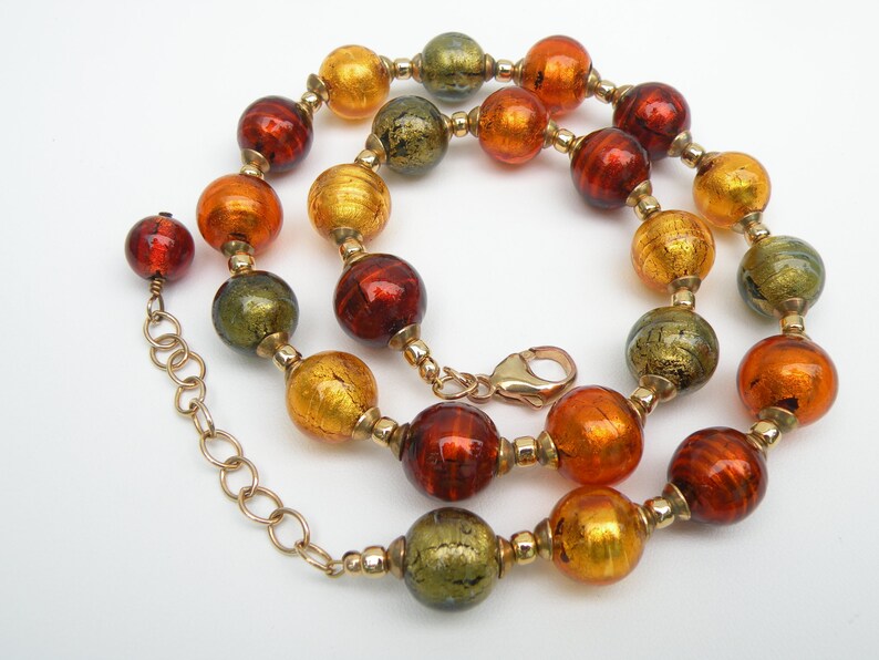 May include: A gold chain necklace with large, round, multi-colored glass beads. The beads are in shades of orange, red, and green with gold flecks.
