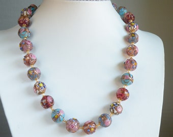 May include: A necklace made of large, colorful glass beads. The beads are round and have a floral pattern. The necklace is strung on a gold chain.