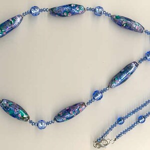 May include: A blue and purple glass bead necklace with a silver clasp. The necklace features a variety of blue and purple beads, including some with floral patterns.