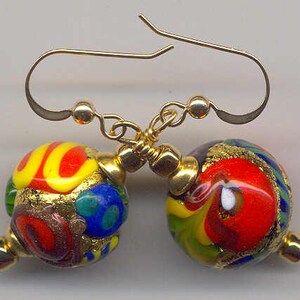 May include: A pair of colorful Murano glass earrings. Each earring features a round, multi-colored bead with red, yellow, blue, and green swirls, accented with gold-colored metal. The earrings have gold-colored ear wires and small gold beads.