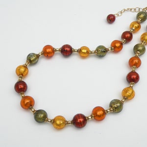 May include: A gold chain necklace with round, multi-colored glass beads. The beads are a mix of orange, red, and green with gold flecks.