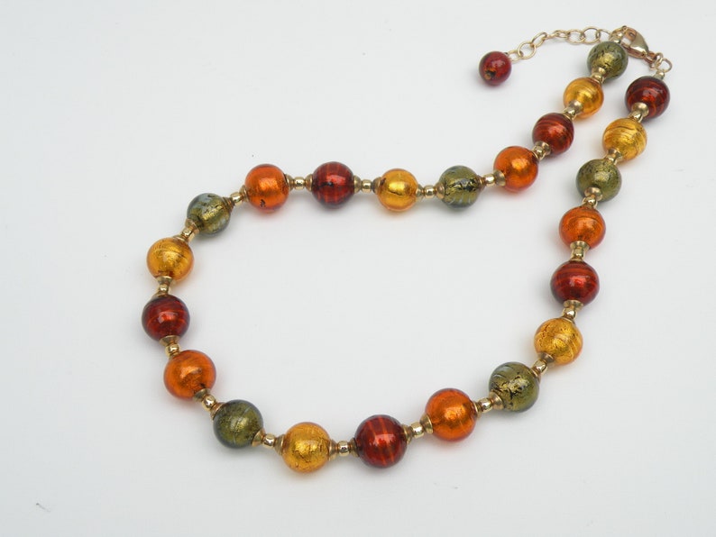 May include: A gold chain necklace with round, multi-colored glass beads. The beads are a mix of orange, red, and green with gold flecks.
