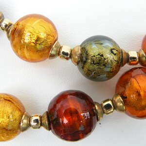 May include: A necklace made of large, round glass beads in shades of gold, brown, and green. The beads have a metallic sheen and are separated by gold-toned metal spacers.