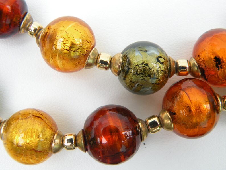 May include: A necklace made of large, round glass beads in shades of gold, brown, and green. The beads have a metallic sheen and are separated by gold-toned metal spacers.