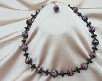 May include: A necklace and matching pendant featuring round, patterned beads in shades of black, brown, blue, and pink. The beads are interspersed with smaller black beads and gold-toned accents, creating a vintage aesthetic.