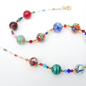 May include: A vibrant necklace with a selection of glass beads in red, blue, green, and gold. The beads are interspersed with smaller, faceted crystals and connected by gold-coloured metal chain. The necklace has a lobster clasp closure.