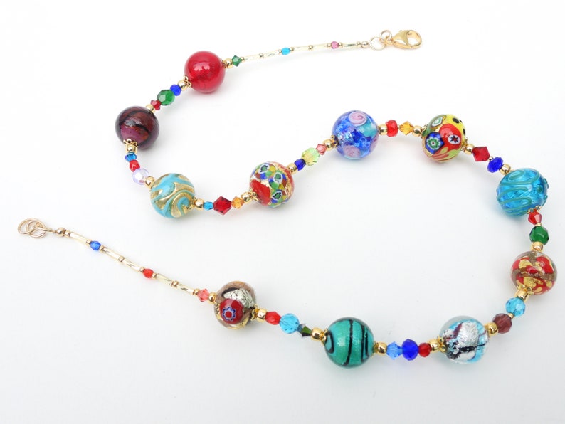 May include: A vibrant necklace with a selection of glass beads in red, blue, green, and gold. The beads are interspersed with smaller, faceted crystals and connected by gold-coloured metal chain. The necklace has a lobster clasp closure.
