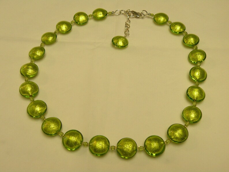 May include: A green glass bead necklace with a silver clasp. The beads are round and have a metallic sheen.