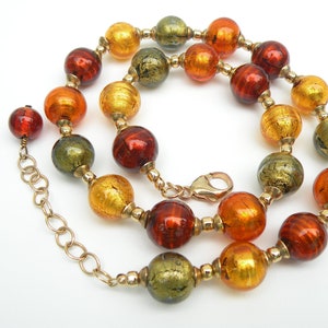 May include: A gold chain necklace with large, round, multi-colored glass beads. The beads are in shades of orange, red, and green with gold flecks.