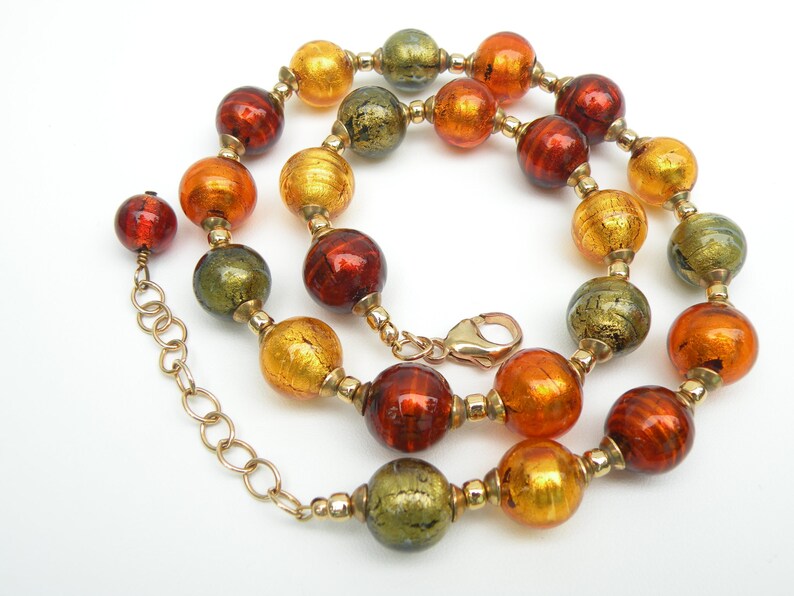 May include: A gold chain necklace with large, round, multi-colored glass beads. The beads are in shades of orange, red, and green with gold flecks.
