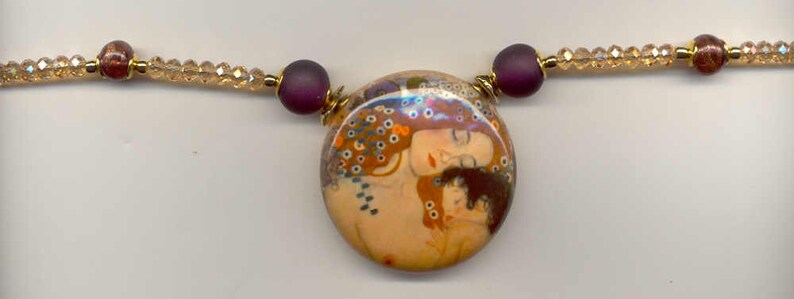 Puede incluir: Collar con un colgante redondo que representa a dos mujeres en tonos c&aacute;lidos. El colgante se complementa con cuentas moradas y una hebra de peque&ntilde;as cuentas doradas brillantes. El collar es una joya art&iacute;stica.