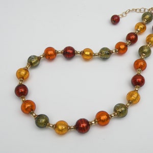 May include: A gold chain necklace with round, multi-colored glass beads. The beads are in shades of green, orange, and red.