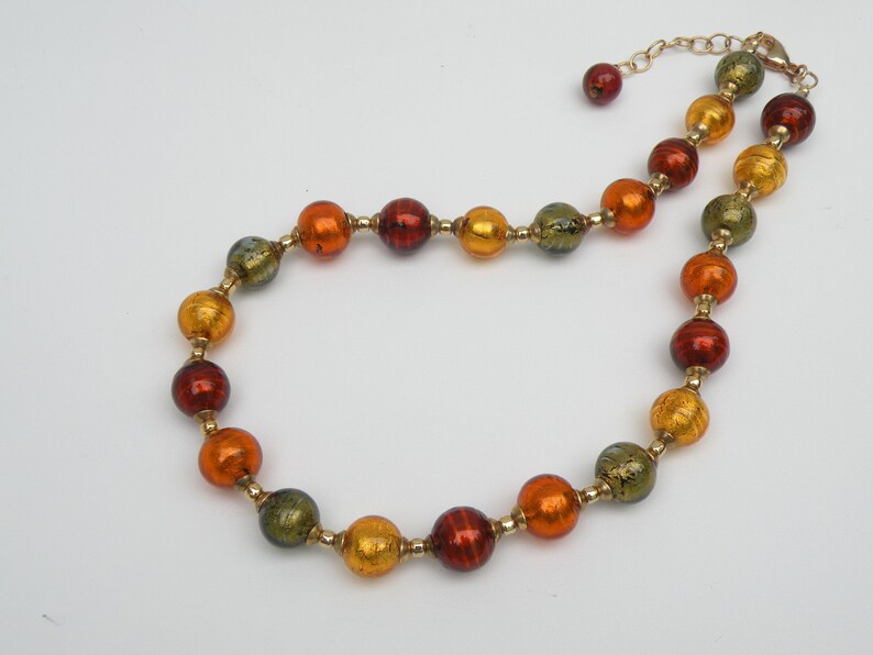 May include: A gold chain necklace with round, multi-colored glass beads. The beads are in shades of green, orange, and red.