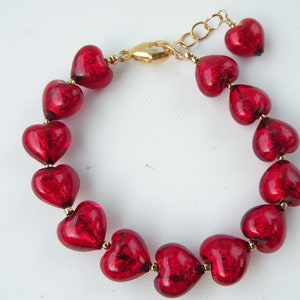 May include: A red heart-shaped glass bead bracelet with a gold clasp. The beads are made of Murano glass and have a shiny, iridescent finish.