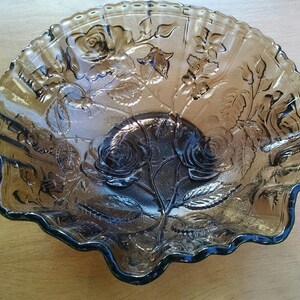 May include: A large, clear glass serving bowl with a scalloped edge. The bowl is decorated with an embossed floral design in a dark brown color.