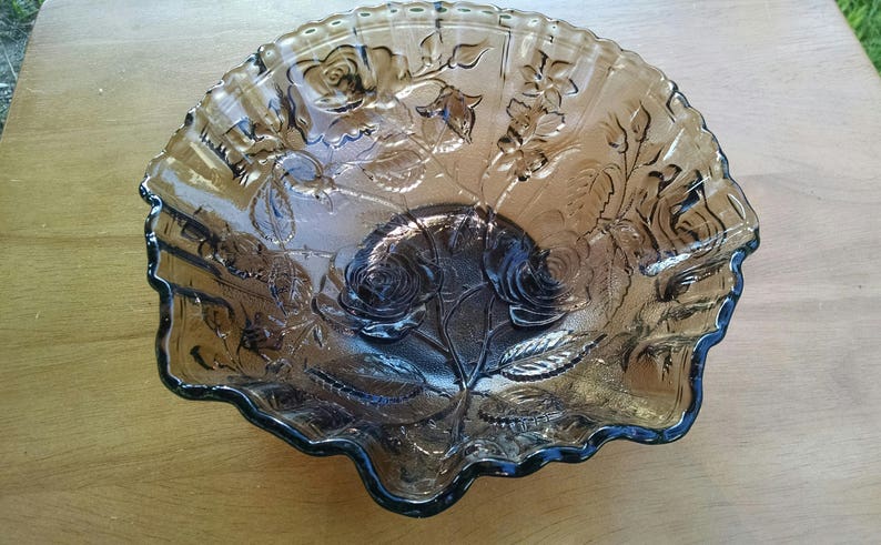 May include: A large, clear glass serving bowl with a scalloped edge. The bowl is decorated with an embossed floral design in a dark brown color.