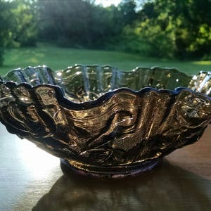 May include: A large, clear glass bowl with a ruffled edge and a textured, floral design. The bowl is made of iridescent glass and has a dark purple hue.